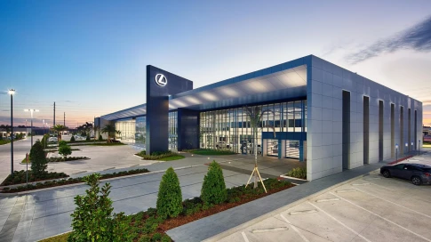 Modern Lexus automotive dealership with glass facade at sunset, landscaped parking area